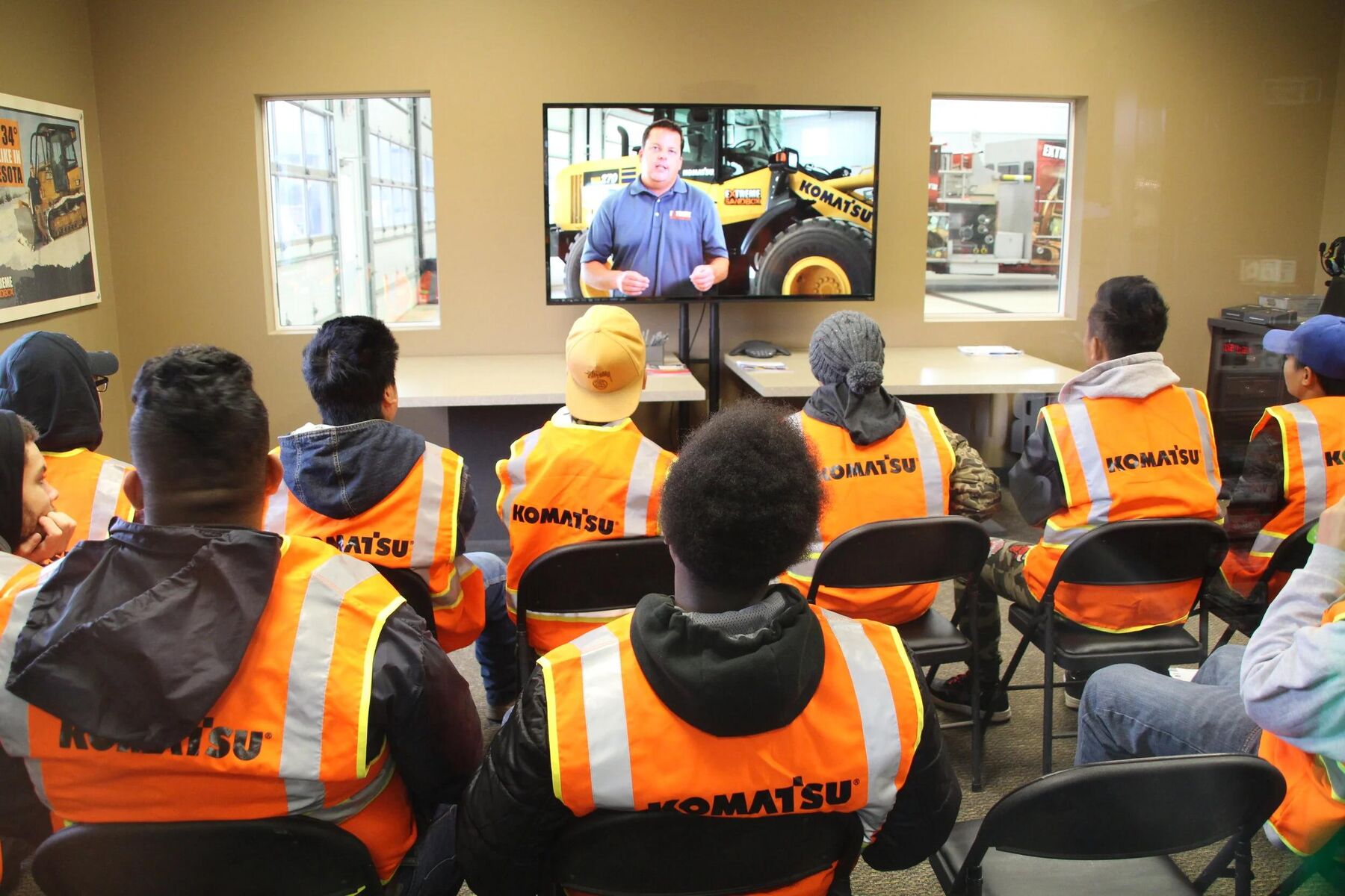 Trainees in high-visibility vests watching a video lesson about heavy equipment